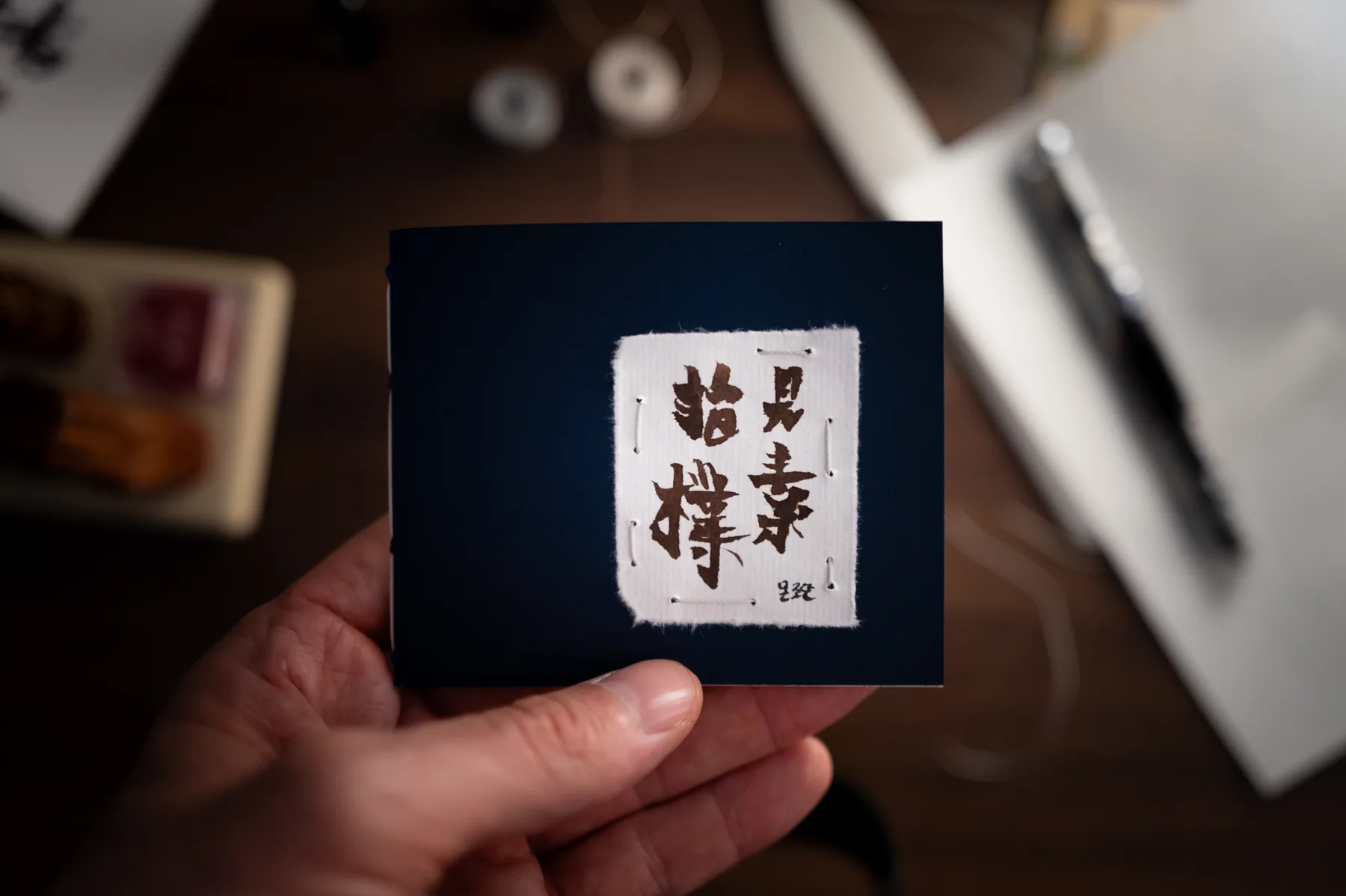 A small blue notebook with a hand-torn piece of hanji stitched to its cover and painted with calligraphy