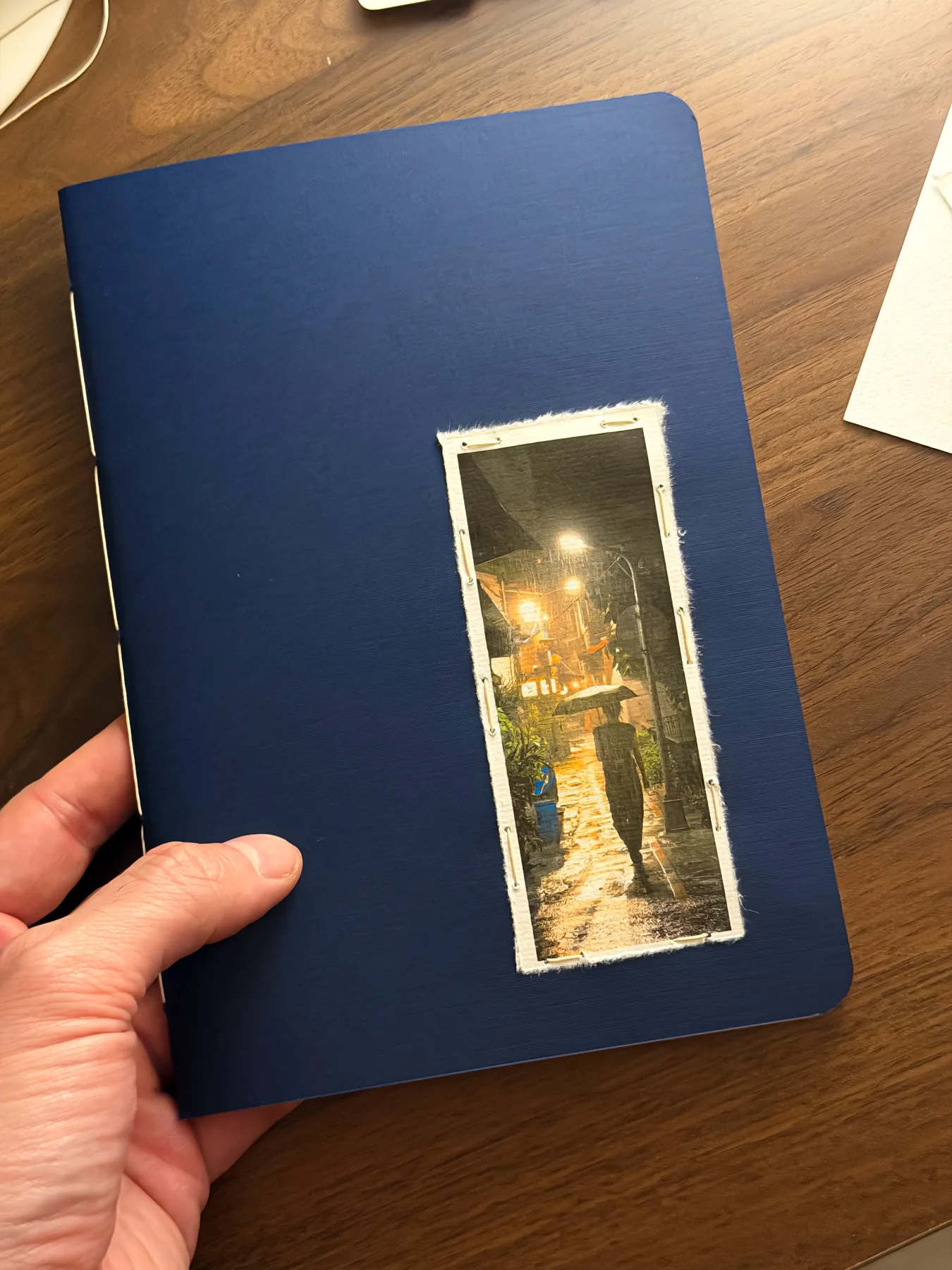A large blue notebook with a narrow photograph sewn onto its cover over a deckled white paper panel
