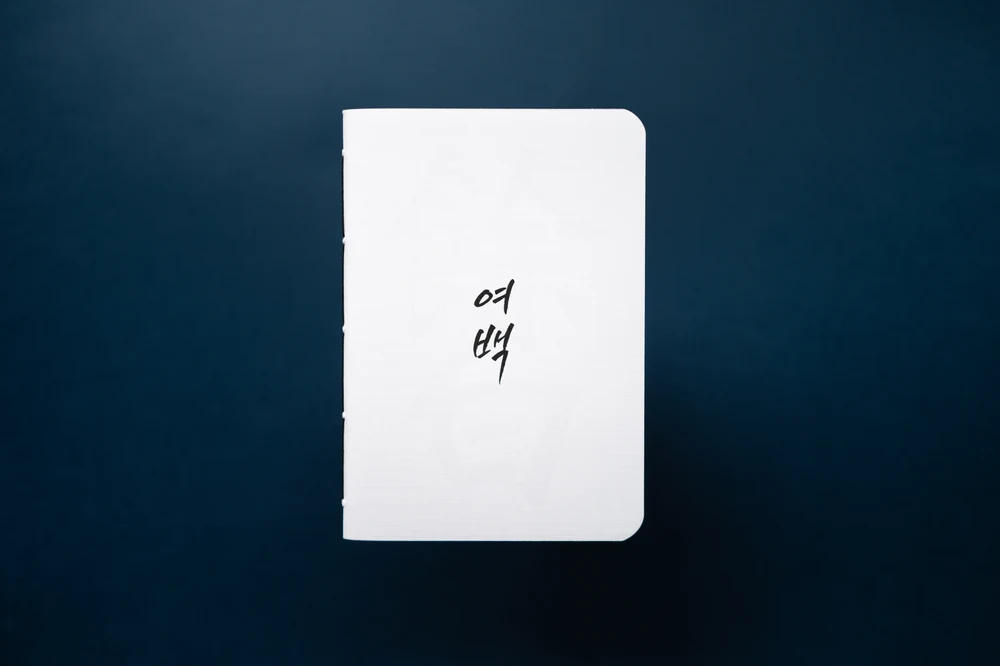 남색 배경 위에 놓인, 한글 서예가 담긴 길쭉한 흰색 여백 노트